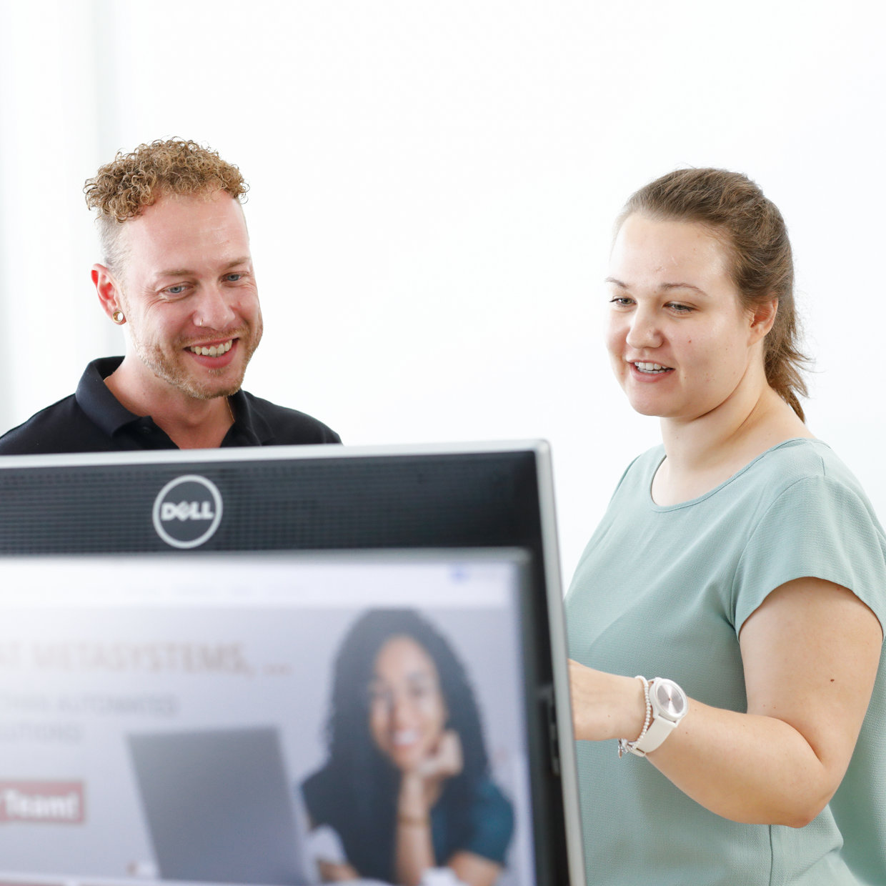 Two colleagues collaborating in front of a computer screen in a bright office, smiling and engaged in discussion.